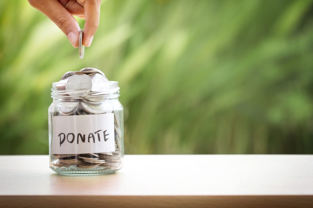 Hand,Putting,Coins,In,Glass,Jar,For,Giving,And,Donation